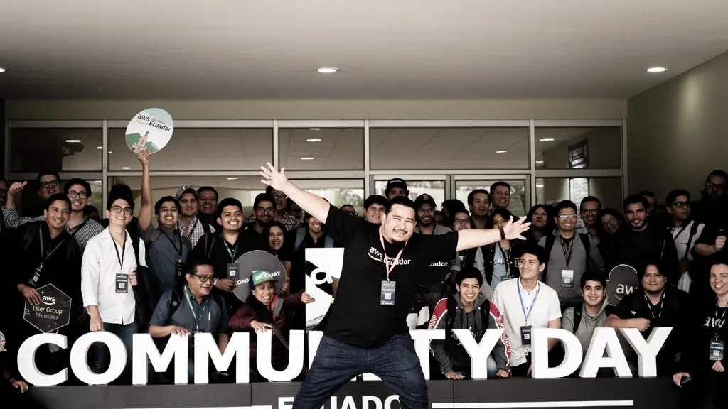 Alexis Polo, líder fundador de AWS User Group Ecuador, celebra saltando junto a decenas de asistentes frente al letrero gigante de AWS Community Day Ecuador